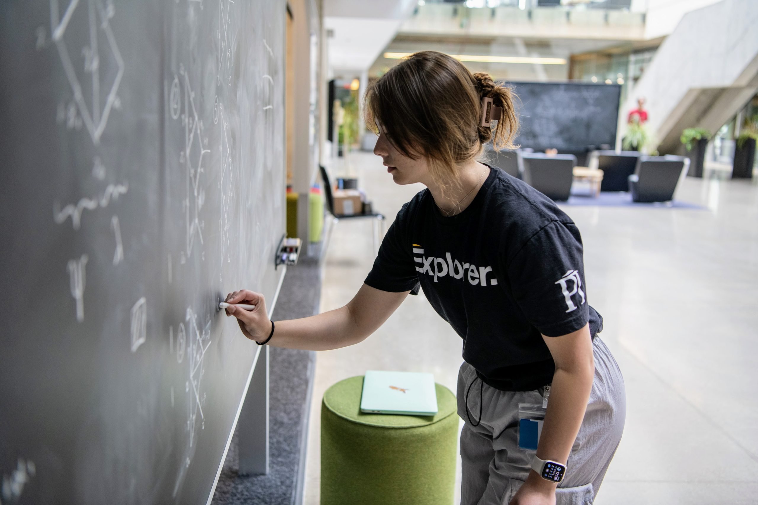 a woman wearing a t-shirt that says Explorer writing on a blackboard