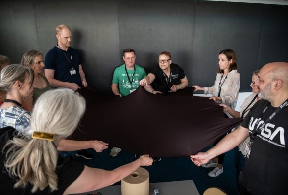 a group of people in a circle with a piece of fabric stretched between them